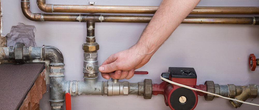Plumber adjusting a valve on a residential plumbing system with copper and steel pipes, showcasing professional maintenance and repair work.