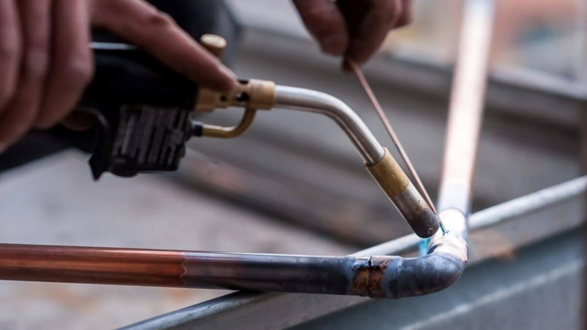 A person using a blowtorch to solder copper pipes during plumbing installation.